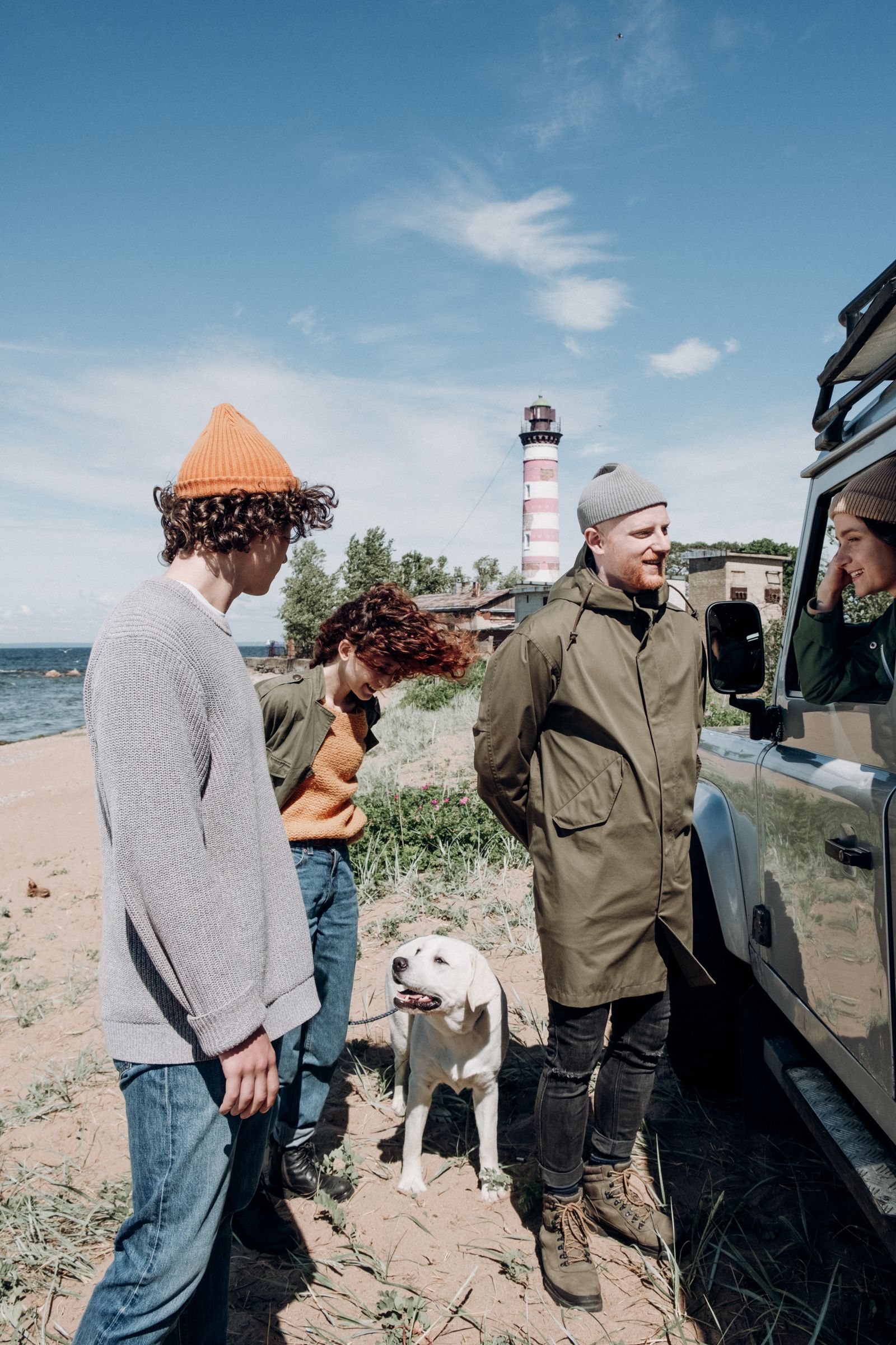 Group of friends with a dog at a beach near a lighthouse, enjoying a sunny day.